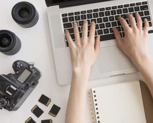 person-s-hand-typing-laptop-keyboard-with-camera-accessories-spiral-book